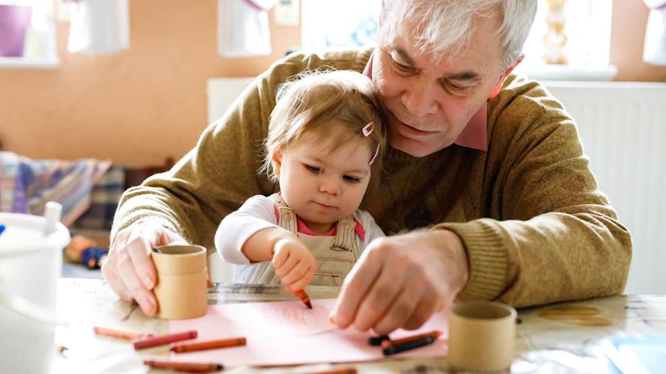 Cute little baby toddler girl and handsome senior grandfather painting with colorful pencils at home.
