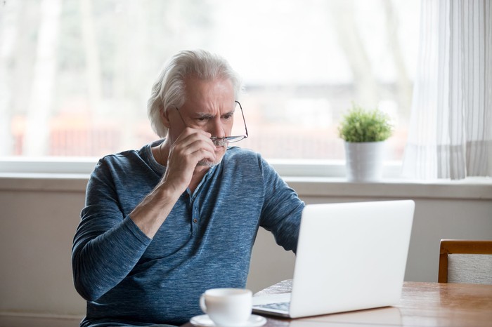 Shocked senior man removing glasses to stare at laptop