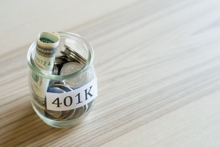 A glass jar filled with bills and coins labeled 401(k).