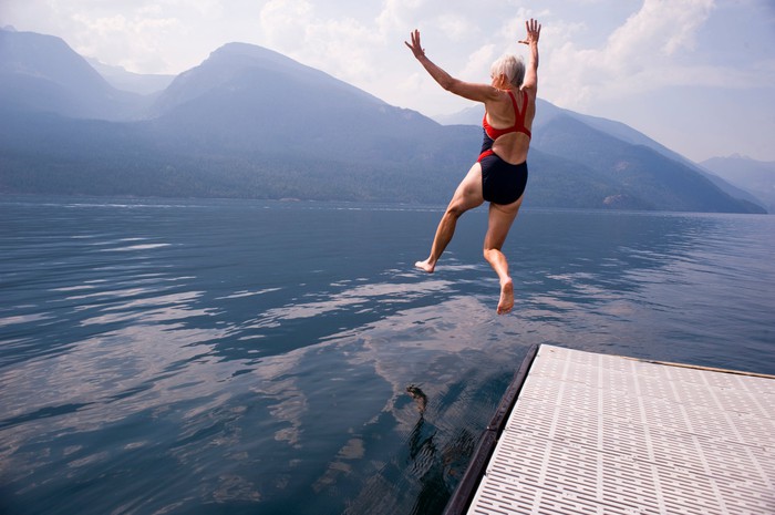 Senior woman jumping into lake.